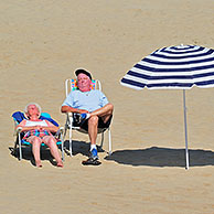 Bejaarde zonnebaders naast parasol op het strand van Koksijde, België

