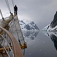 Man op boegspriet van zeilschip kijkt uit over de Lemaire Channel / Kodak Gap, Antarctica
