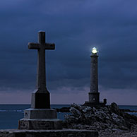 Kruis en de vuurtoren Phare de la Hague bij nacht te Goury, Normandië, Frankrijk
